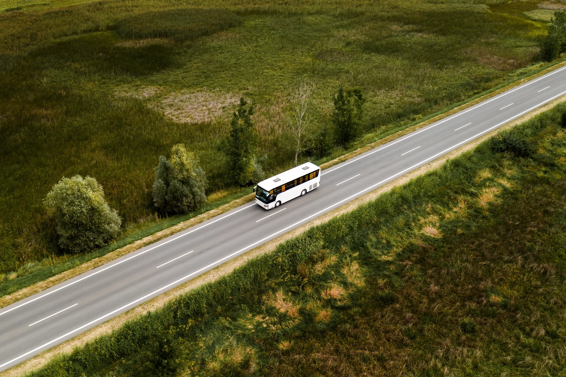 Vue aérienne d'un autocar blanc CDP69 roulant sur une route au milieu de champs verts
